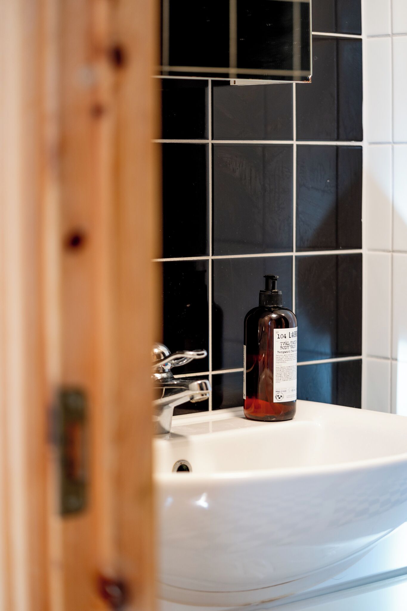 A bathroom with a white sink, a bottle of lotion, and black and white tiled walls.