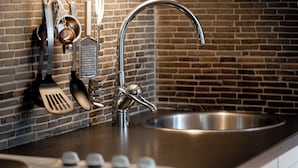 A kitchen with a stainless steel sink, a modern faucet, and various kitchen utensils hanging on the wall.