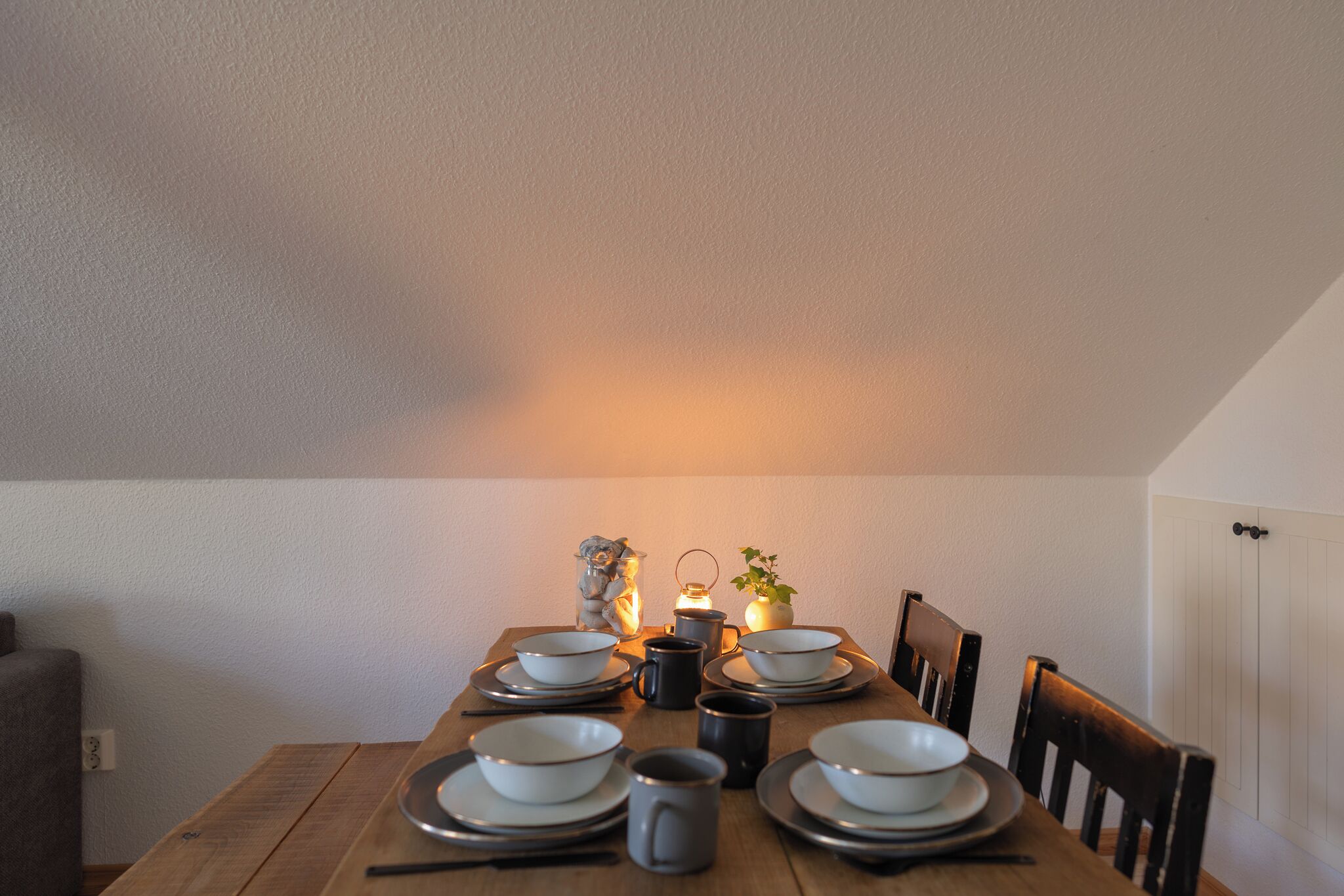 Une table à manger dressée avec des assiettes, des bols et des tasses, agrémentée d’une petite lanterne et d’objets décoratifs.