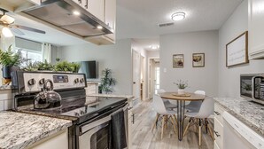 A modern kitchen with a gas stove, oven, and microwave, a dining area with a table and chairs, and a hallway leading to other rooms.