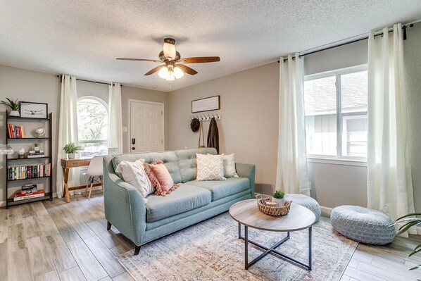 A living room with a blue sofa, a round coffee table, a bookshelf, and a ceiling fan.