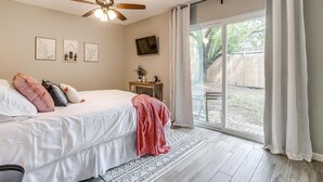 A bedroom with a bed, ceiling fan, and a view of the backyard through a sliding glass door.
