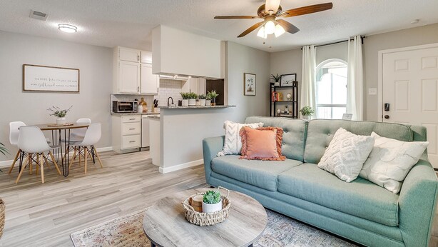 A modern living room with a teal sofa, a coffee table, and a dining area with a white table and chairs.