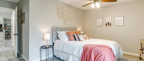 A bedroom with a bed, a ceiling fan, a bedside table, a lamp, and a macrame wall hanging.