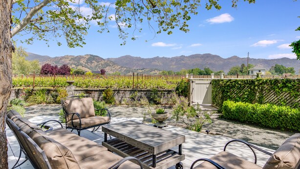 Une terrasse avec des meubles d’extérieur, une table en pierre et une vue sur les vignes et les montagnes.