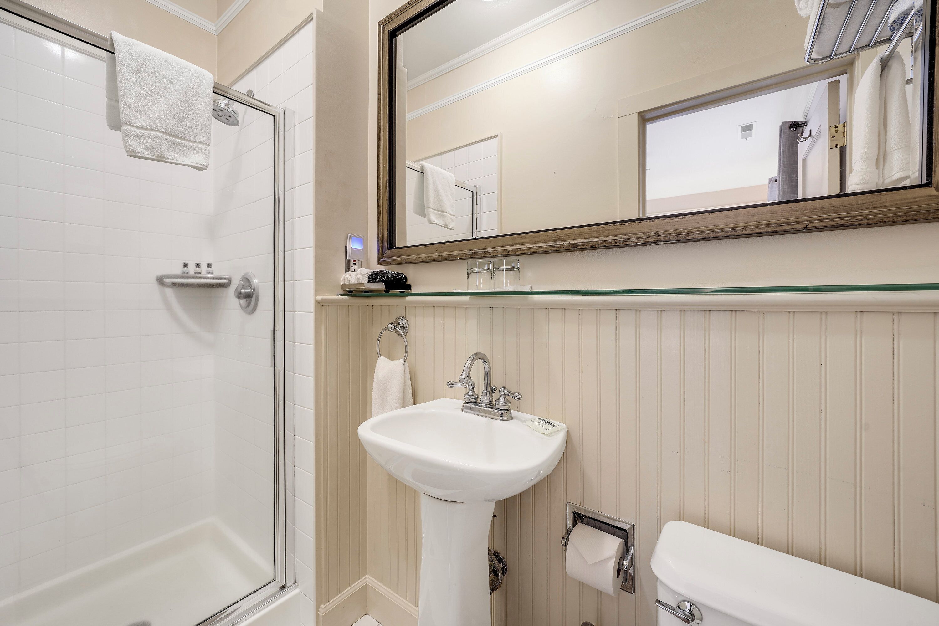 A bathroom with a white sink, a mirror, a toilet, and a shower.