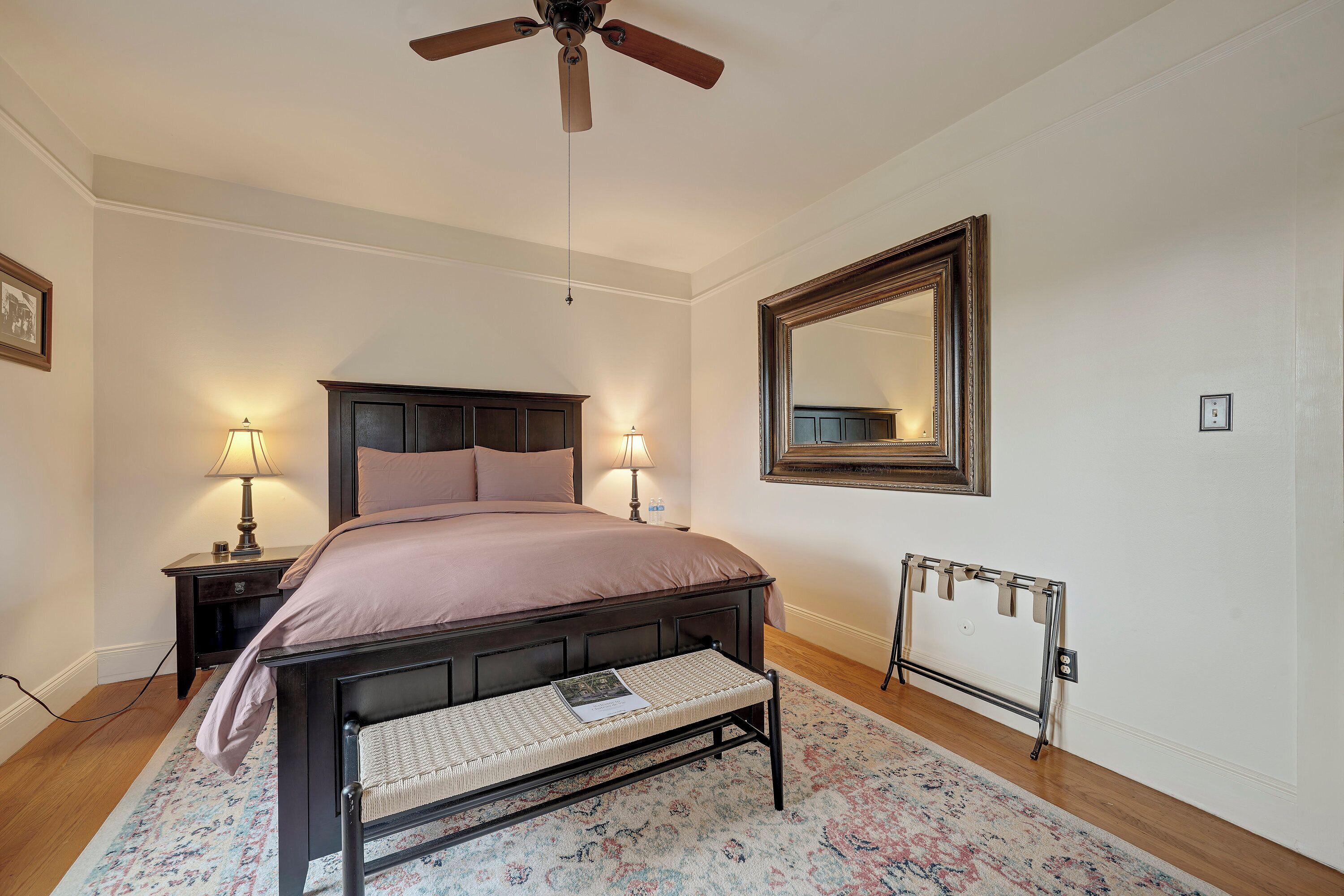Une chambre à coucher avec un lit, des lampes de chevet, un ventilateur de plafond, un grand miroir et un radiateur.