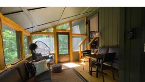 A cozy cabin interior with a sofa, dining table, and chairs, large windows, and a staircase. - Saturdays Cabin, Hot Tub, Hammock, Gas Firepit (pocono lake)