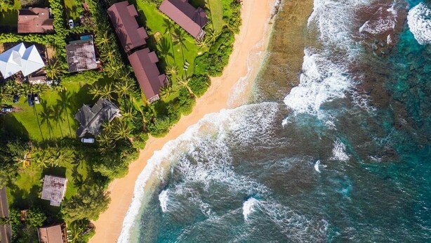 Vista aérea de una propiedad costera con varias casas, una playa y olas del océano.