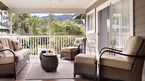 Un espacio al aire libre techado con mobiliario de mimbre, ventilador de techo y vistas a montañas tropicales.