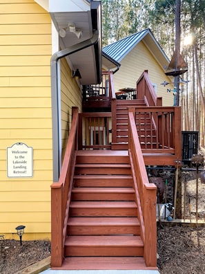 Un escalier en bois mène à un porche sur lequel est affiché un panneau indiquant : « Bienvenue au Lakeside Landing Retreat ! »