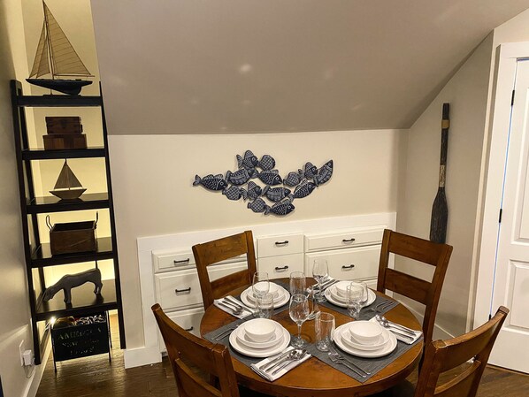 A dining room with a round table set for four, wooden chairs, a decorative fish wall art, a black shelf with various items, and a white cabinet with drawers.