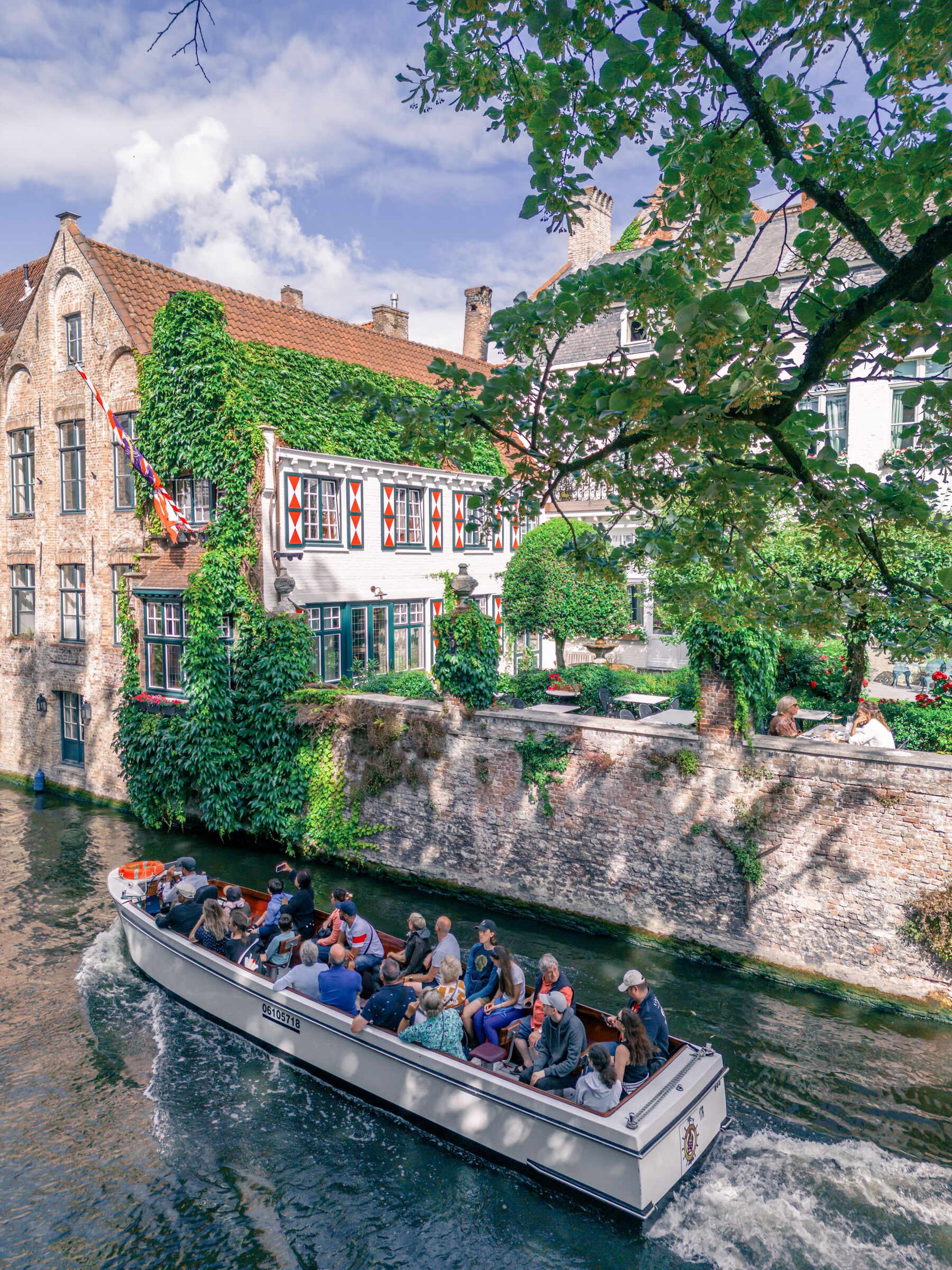 Ein Boot mit Passagieren auf einem Kanal, umgeben von historischen Gebäuden mit roten Ziegeldächern und Efeu bewachsenen Wänden.