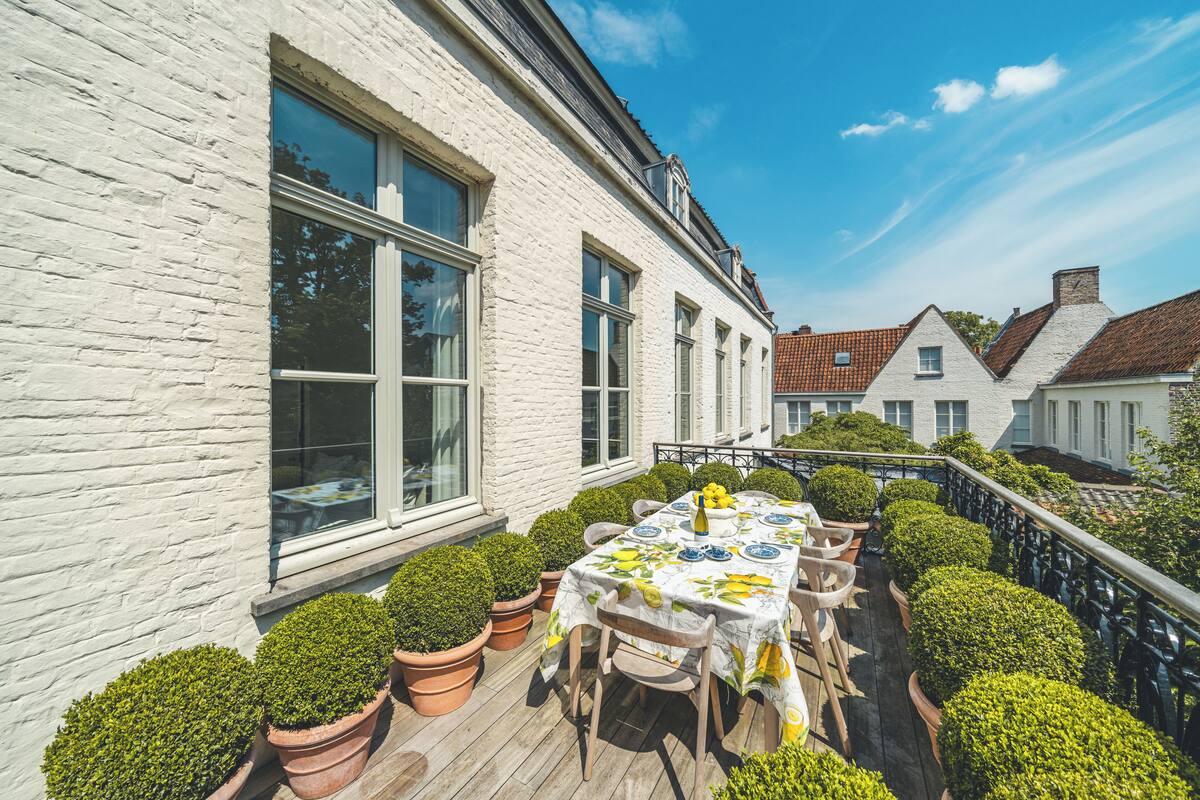 En vit byggnad med en träveranda, krukväxter och ett bord dukat för måltider.