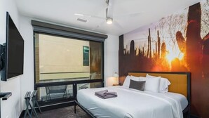 Habitación de hotel con una cama grande, ventana con vistas, ventilador de techo y televisor montado en la pared.