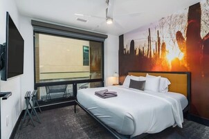 Habitación de hotel con una cama grande, ventana con vistas, ventilador de techo y televisor montado en la pared.