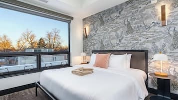 A modern hotel room with a large bed, a view of the outside, and a patterned wallpaper.