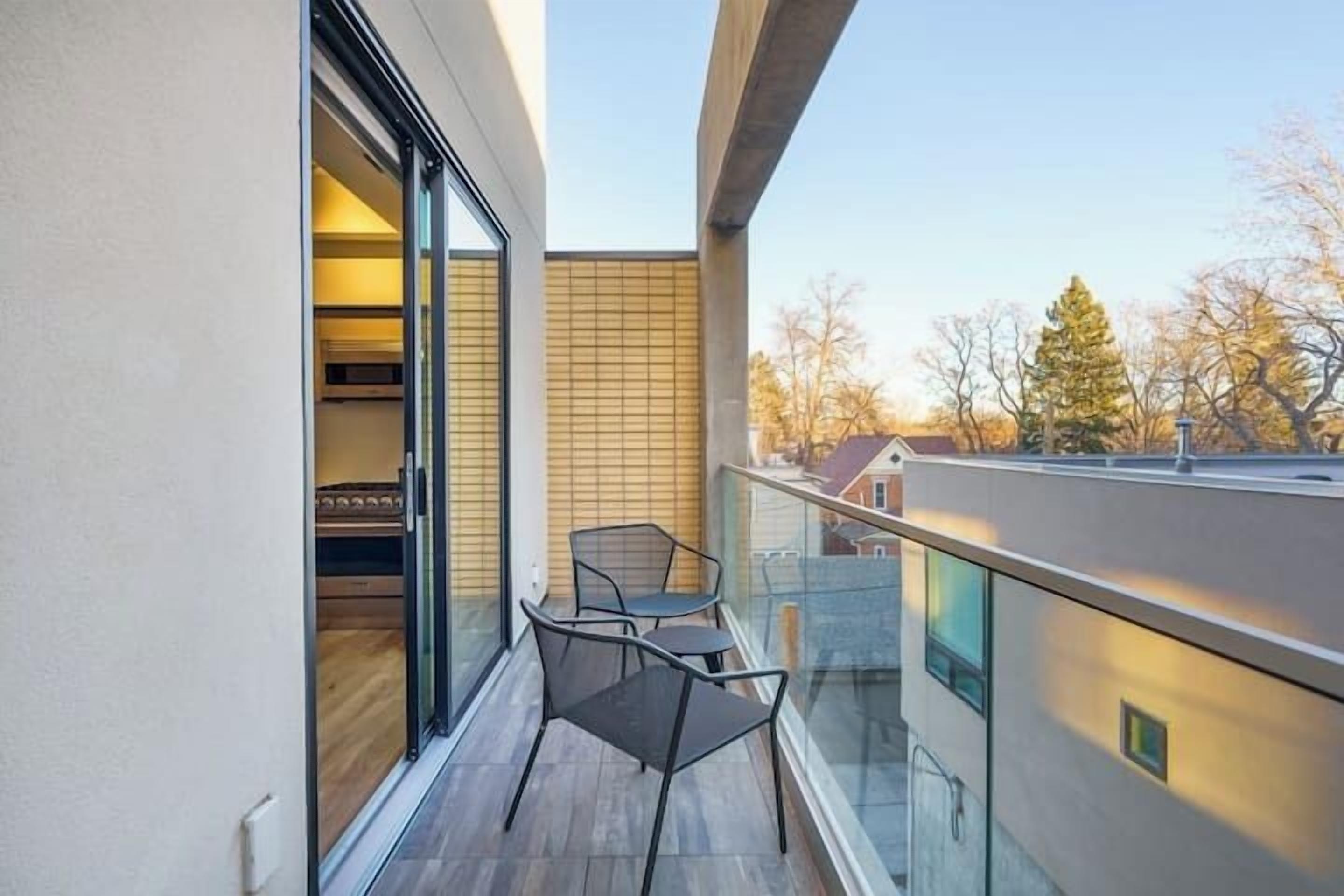 A balcony with a glass railing, two chairs, and a view of the cityscape.