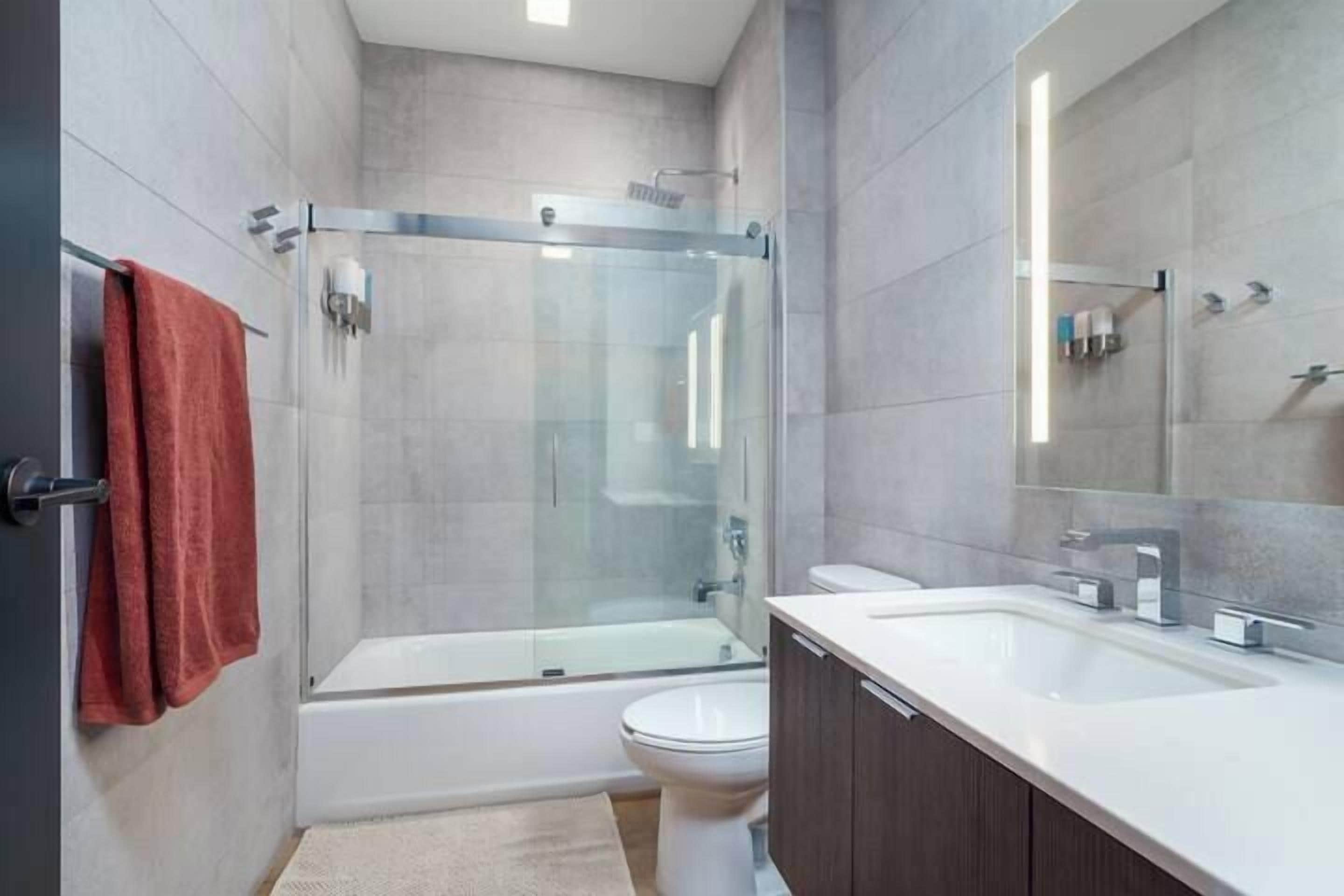 Une salle de bain moderne avec une douche à parois de verre, des toilettes blanches et un grand miroir.