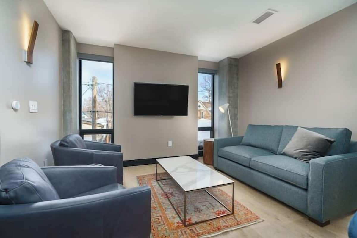Uma sala de estar moderna com um sofá, poltronas, uma mesa de centro e uma TV fixada na parede.