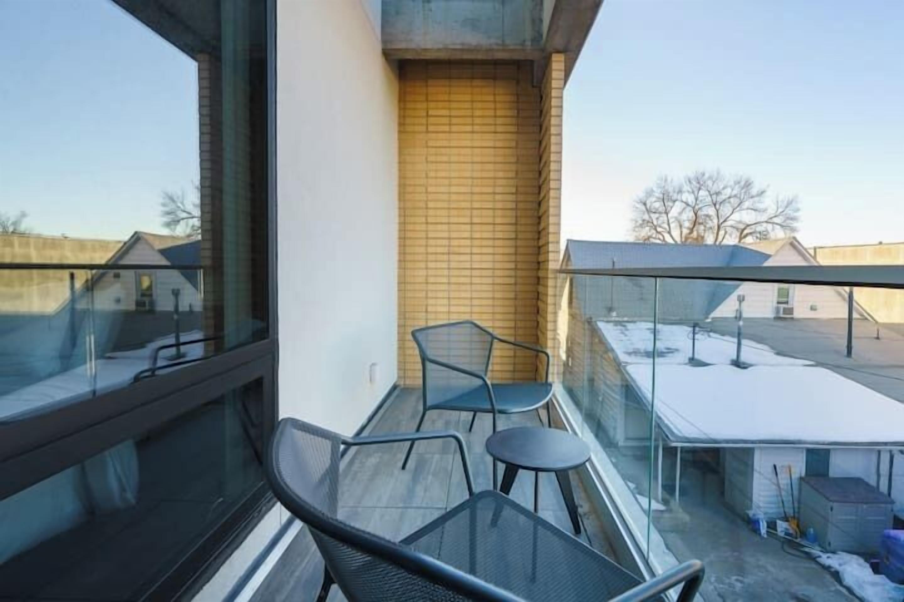A balcony with a glass railing, two chairs, and a small table.