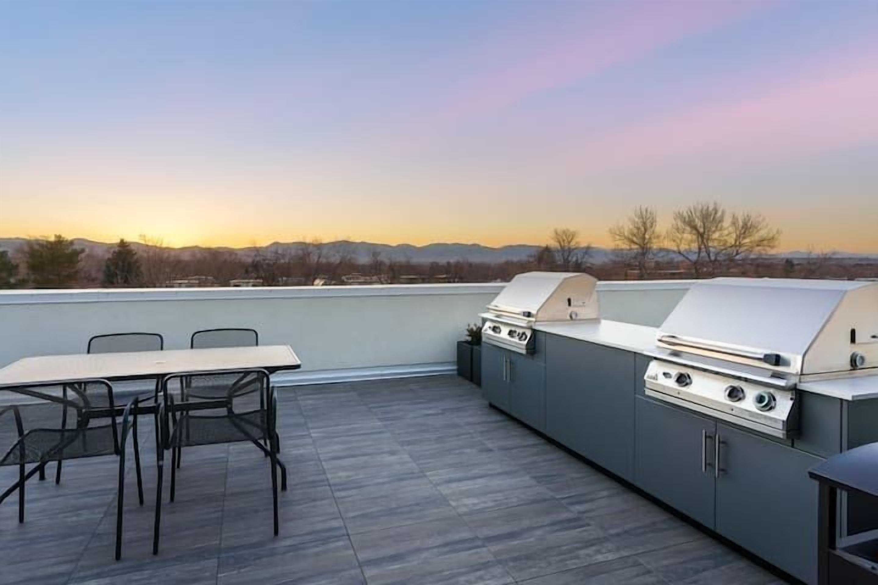 An outdoor patio with a grill and table, overlooking a mountainous landscape.