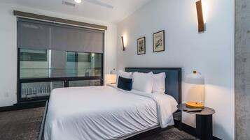 Una habitación de hotel con una cama, una lámpara de pie, un ventilador de techo y un ventanal con persianas.