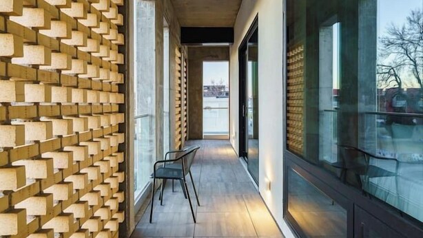 Un pasillo con un papel tapiz decorativo, una silla y ventanas amplias.