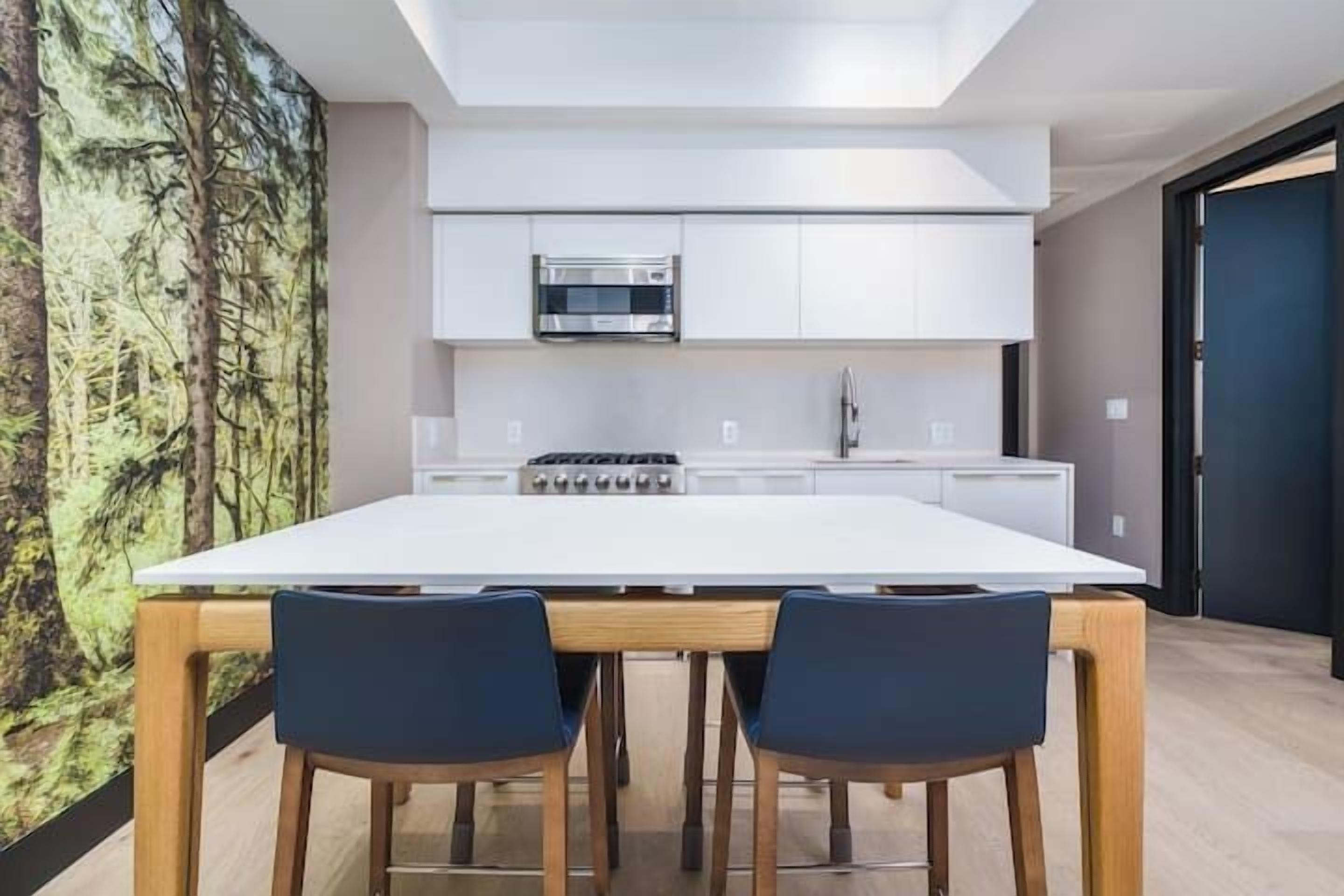 A modern kitchen with white cabinets, a built-in oven, and a large island with two chairs.