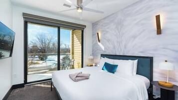 Una habitación de hotel moderna con una cama grande, un ventilador de techo, vistas al exterior y una pared de mármol.