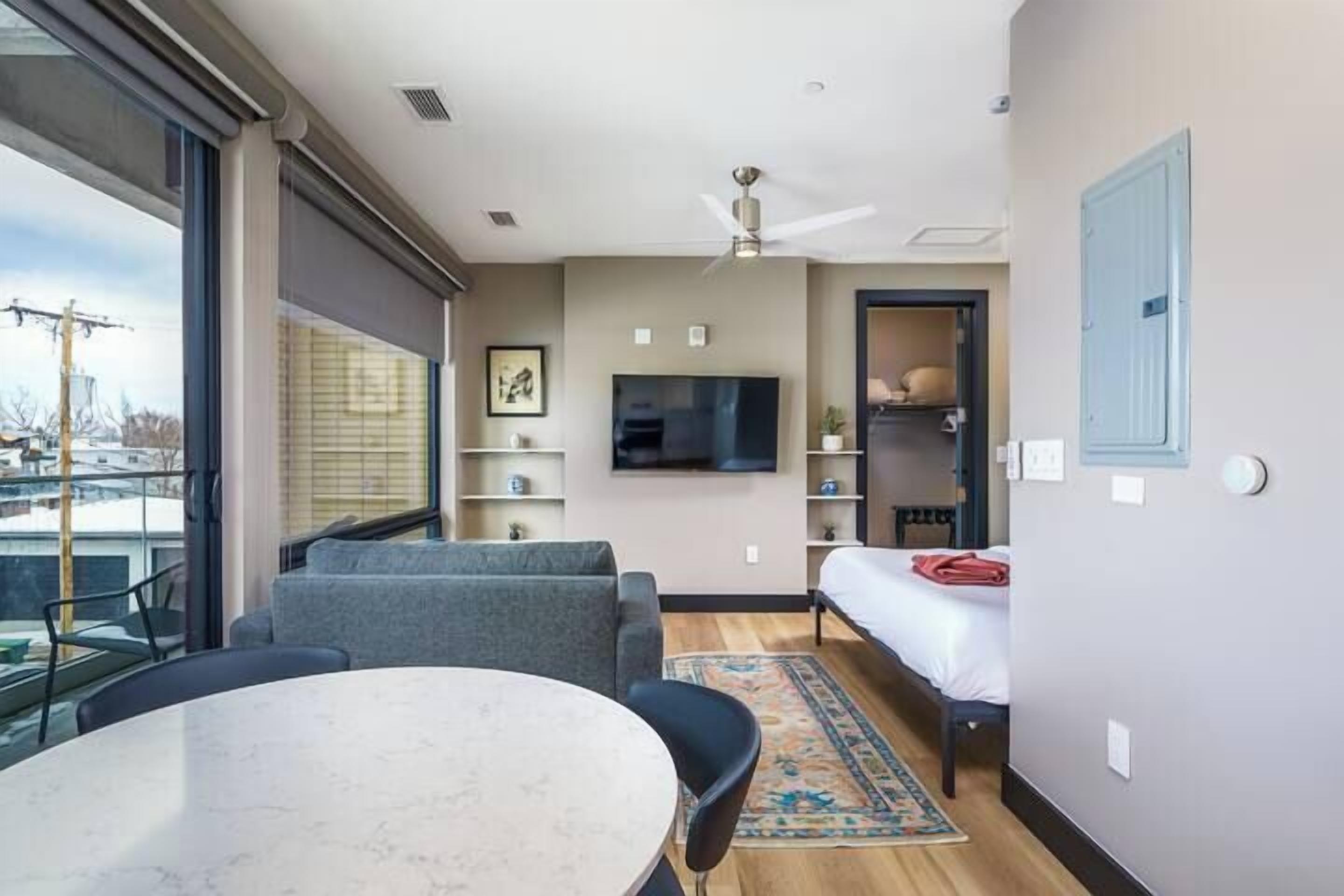 Ett modernt hotellrum med ett stort fönster, en platt-TV, en soffa, ett matbord och en säng.