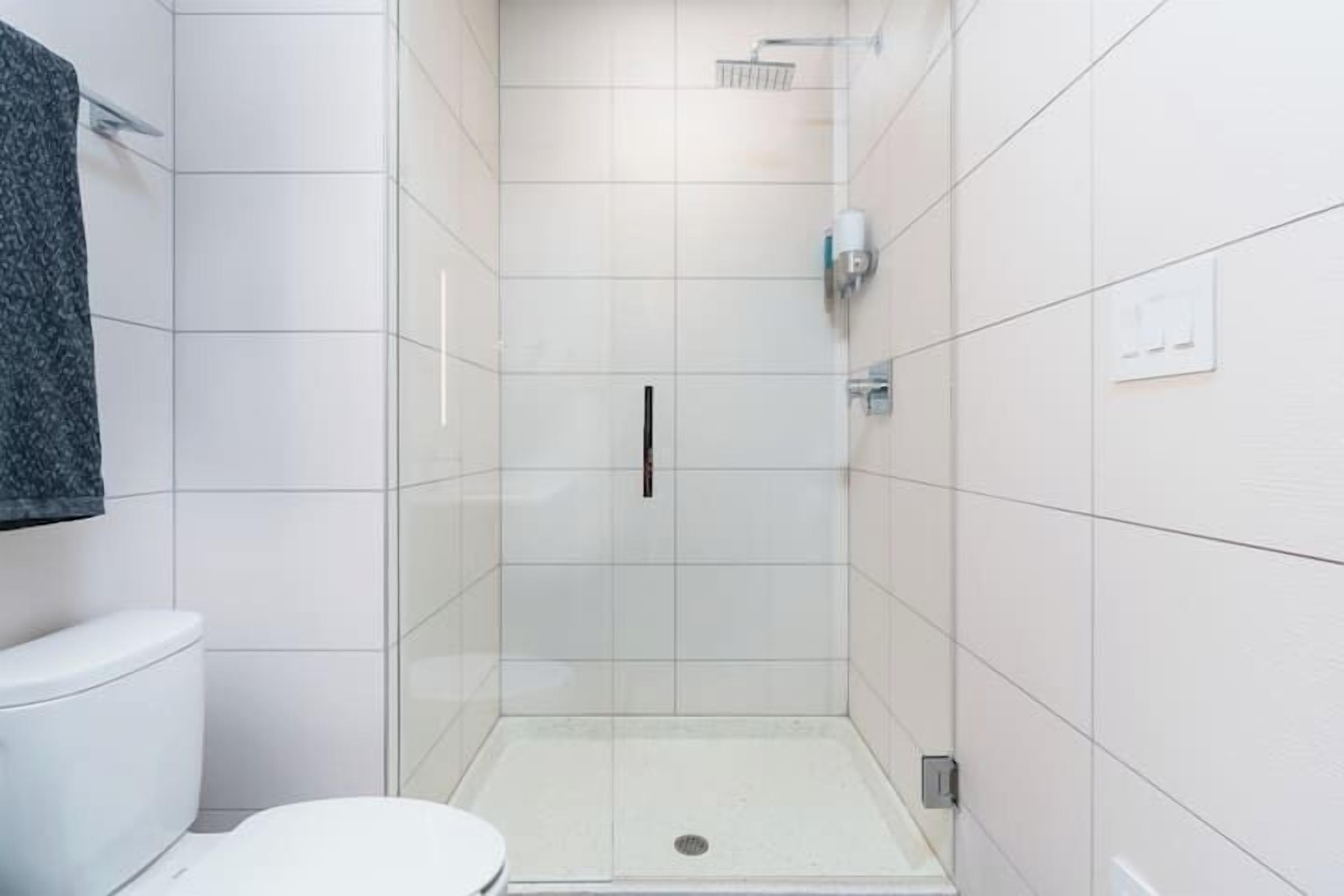 A modern bathroom with a white tiled shower enclosure, a toilet, and a towel rack.