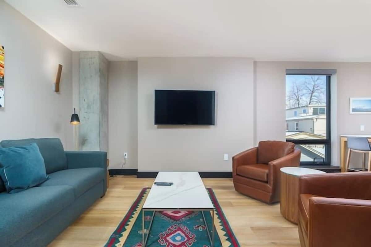 Uma sala de estar moderna com sofá, mesa de centro e televisão na parede.