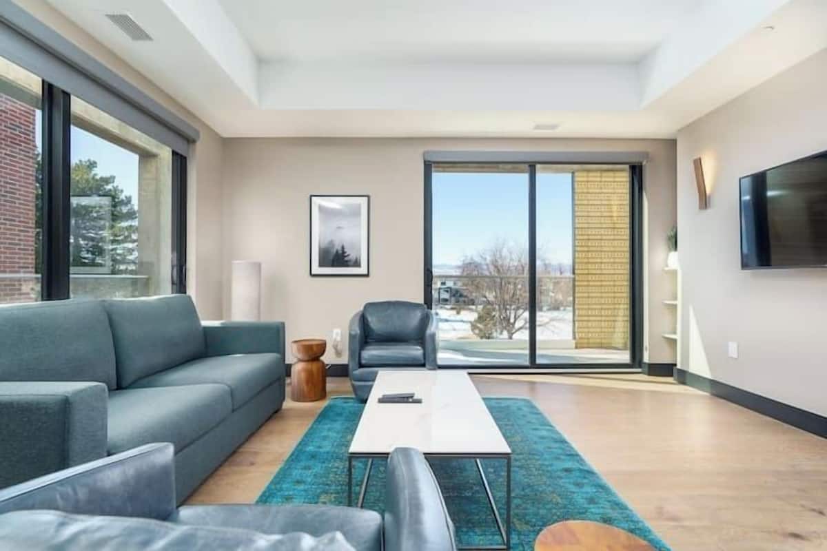 Uma sala de estar moderna com um sofá, uma mesa de centro e uma poltrona. Há uma janela grande com vista para o exterior.