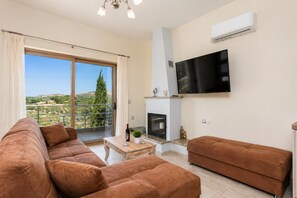 Ein Wohnzimmer mit einer Couch, einem Couchtisch, einem Kamin und einem an der Wand montierten Fernseher.