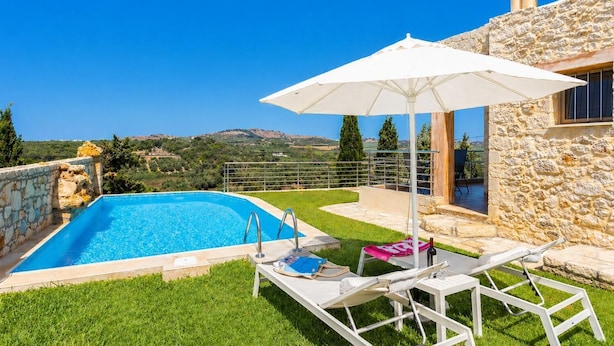Une piscine bordée d’un mur en pierre, un parasol blanc et une vue sur la campagne.