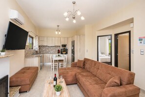A compact living space with a sofa, a dining table, and a kitchen area. - Stefania Villa Dio - One Bedroom Villa, Sleeps 2 (Roumeli)