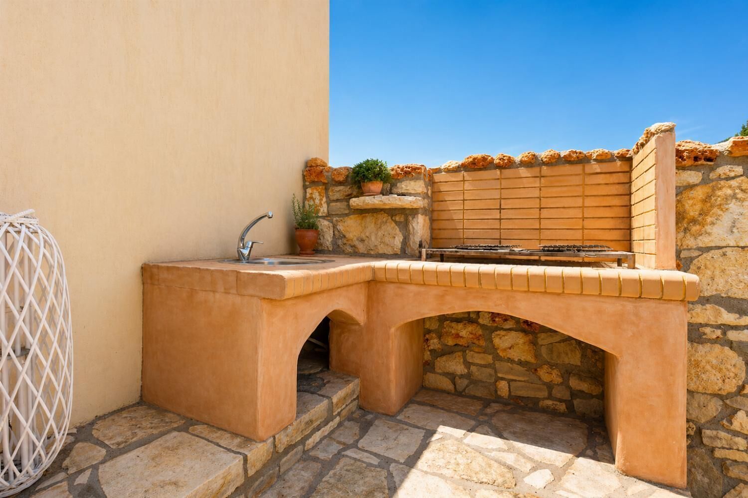 An outdoor kitchen with a sink, a grill, and a stone wall.