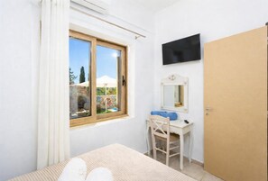 A bedroom with a bed, a desk with a chair, a TV, and a door. - Stefania Villa Dio - One Bedroom Villa, Sleeps 2 (Roumeli)
