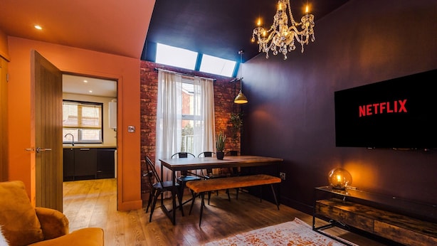A modern living room with a dining area, a TV mounted on the wall, and a chandelier. - 4 Bed Urban Home in Manchester (Manchester)
