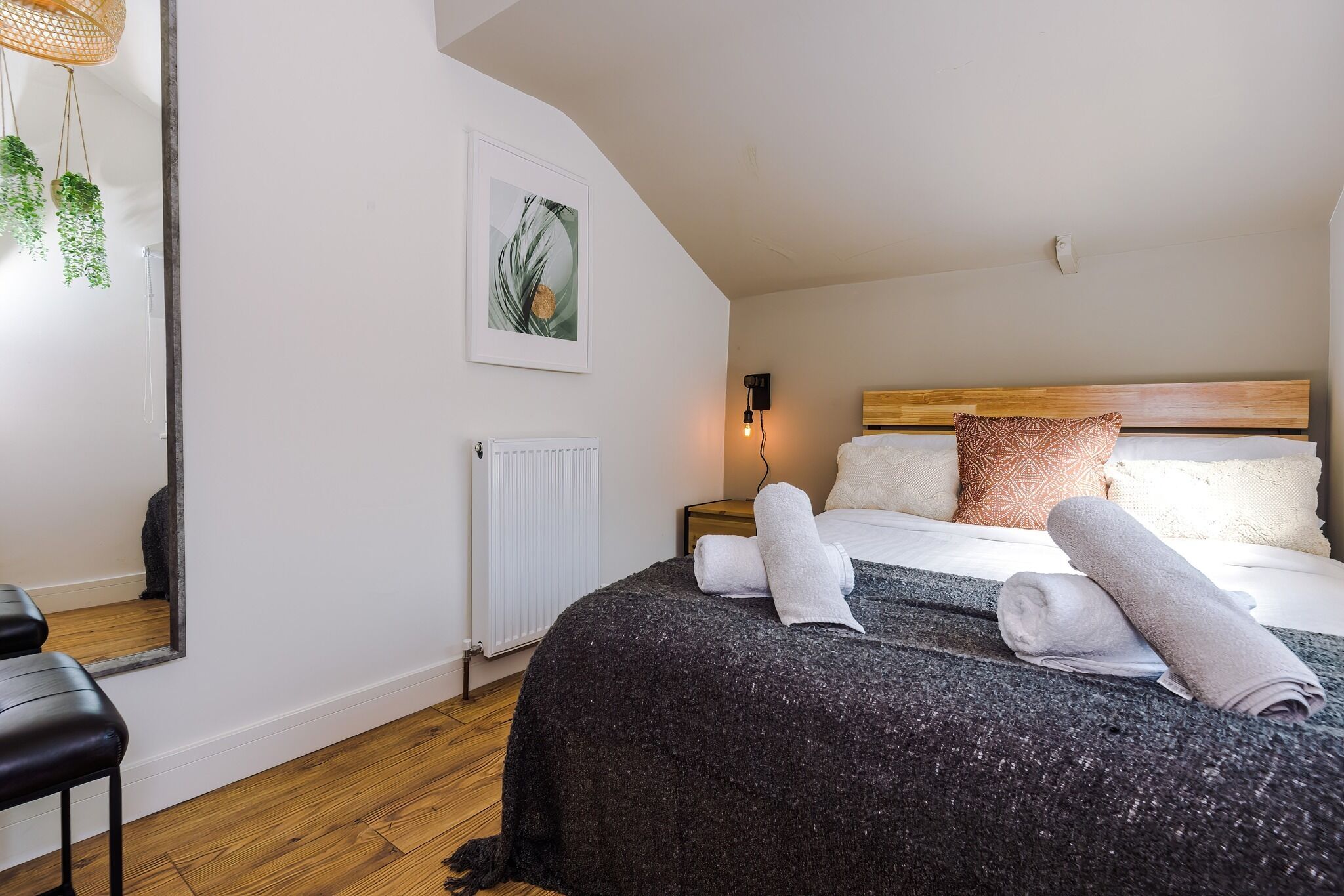 Une chambre à coucher avec un grand lit, une tête de lit en bois, un radiateur, une lampe fixée au mur et un tableau encadré.