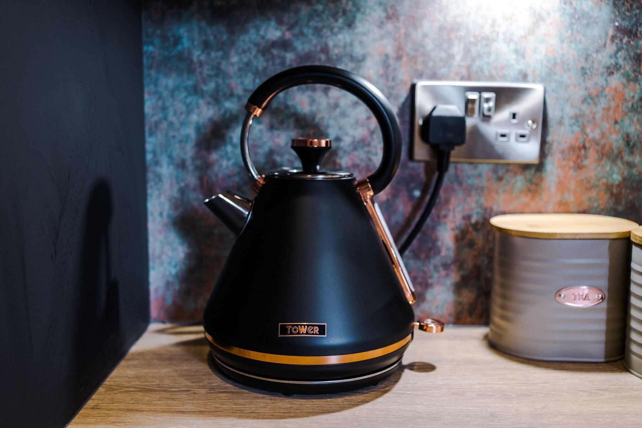 A black kettle with a handle and spout, placed on a wooden surface.