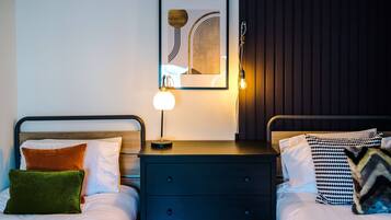 Habitación de hotel con dos camas, una mesita de noche con lámpara, un cuadro enmarcado en la pared y cabecero de madera.