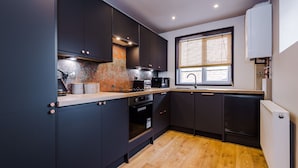 A modern kitchen with dark cabinetry, a wooden countertop, a built-in oven, and a window with blinds. - 4 Bed Urban Home in Manchester (Manchester)