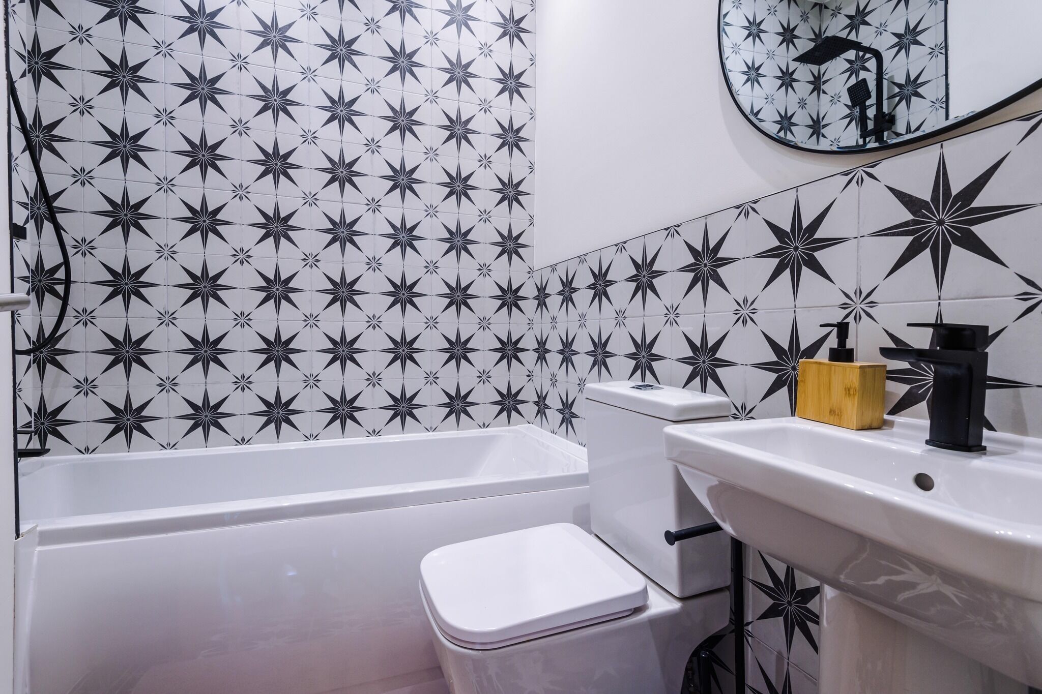 Ein Badezimmer mit Fliesenrückwand in Sternenmuster, einer weißen Badewanne, einer weißen Toilette und einem Waschbecken mit schwarzem Wasserhahn.