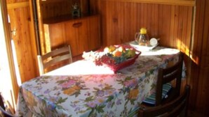 A wooden interior with a table covered by a floral tablecloth, a bowl of fruit, and a pitcher on the table. - Furnished mini-apartment (Bagni di Vinadio)