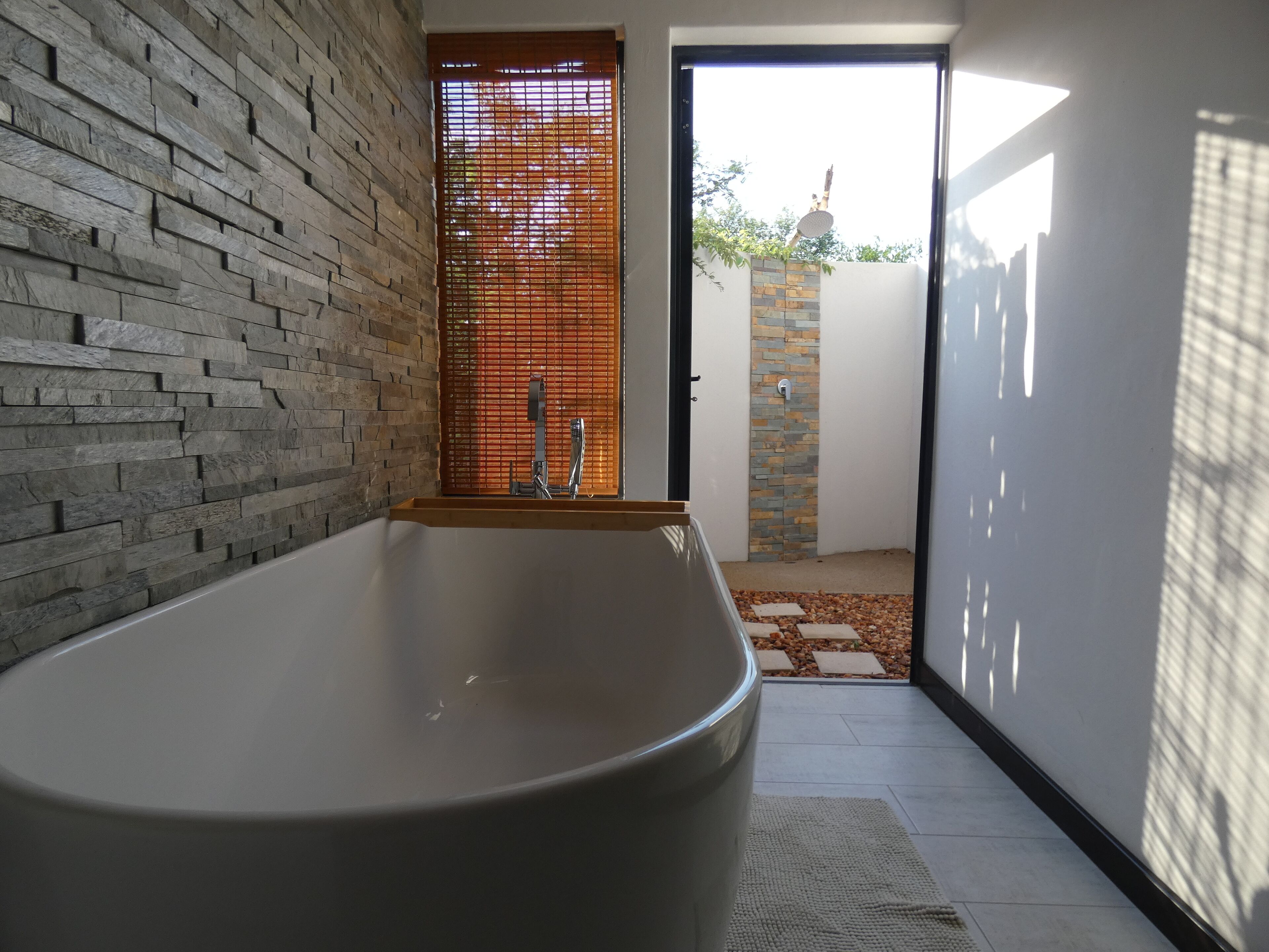 A modern bathroom with a large bathtub, a wooden door with blinds, and a view of the outside.