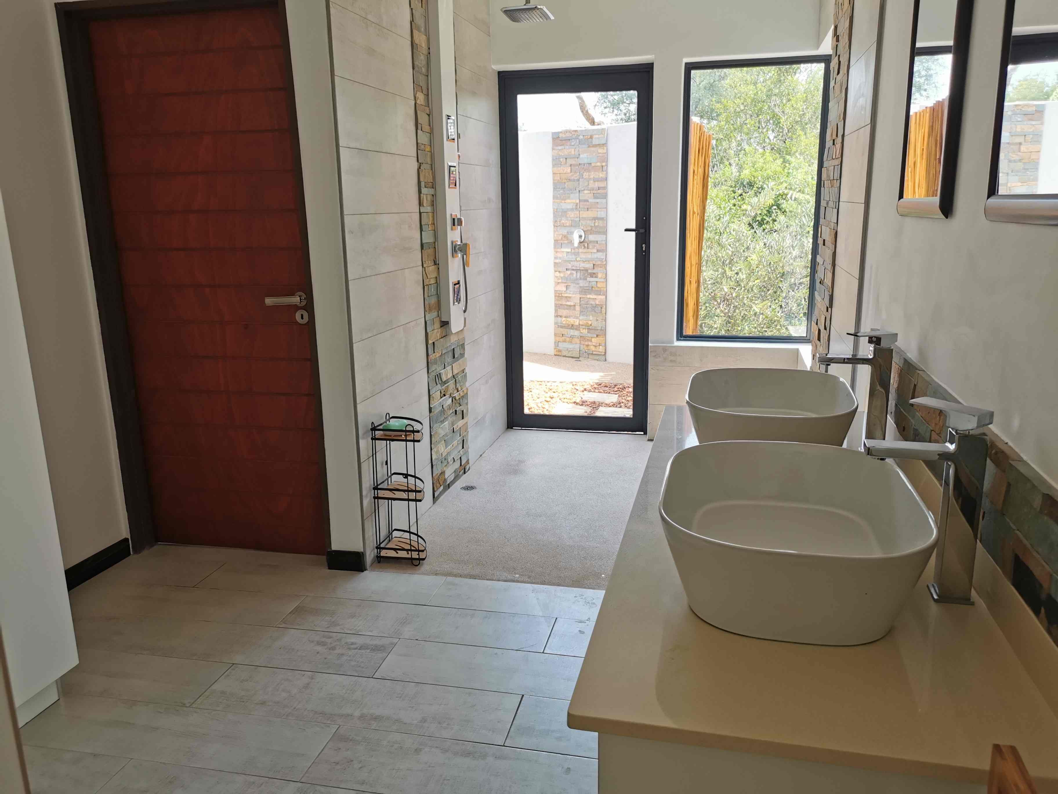 Ein modernes Badezimmer mit zwei großen Waschbecken, einer Holztür und Blick ins Freie.