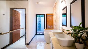 A modern bathroom with a glass shower, a large freestanding bathtub, and a sink with a potted plant.
