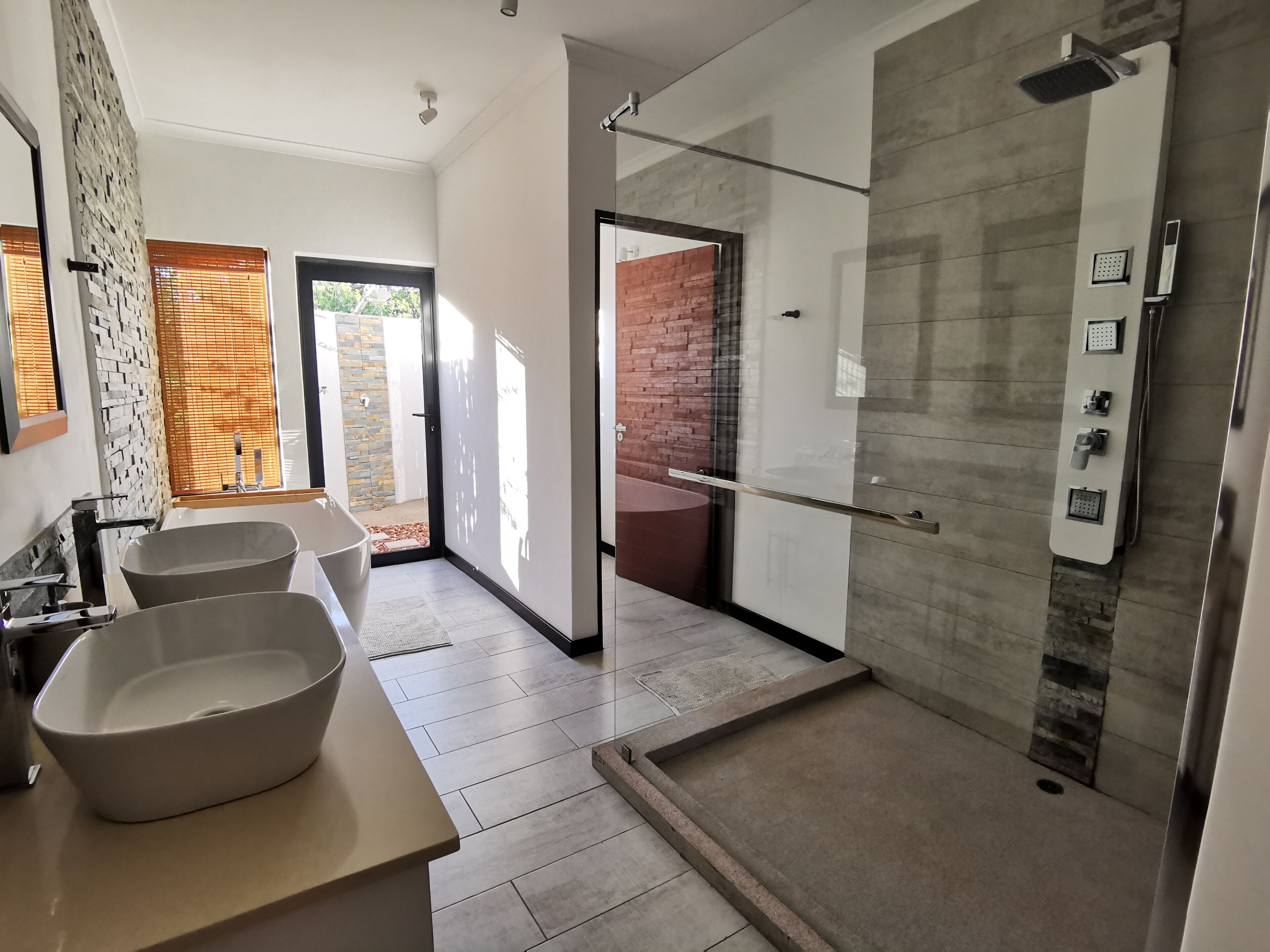 A modern bathroom with two sinks, a glass shower enclosure, and a view to the outside.